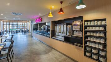 Un café moderno con barra, zona de mesas y exhibición de tazas y platillos.
