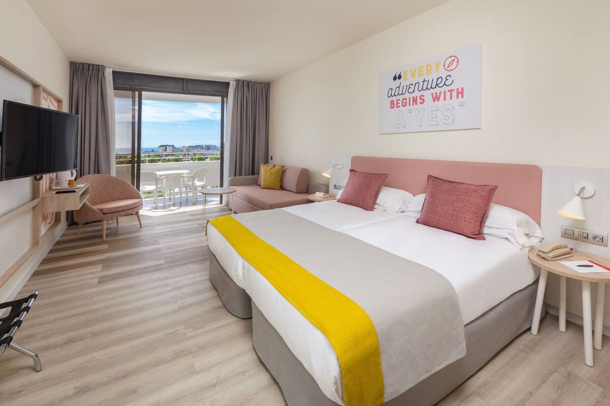 Habitación de hotel con una cama grande, un escritorio con silla, un televisor y un balcón con vistas.