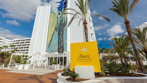 A hotel with a large mural on the facade, palm trees, and a sign for 'Abora - BUENAVENTURA by LOPESAN HOTELS'.