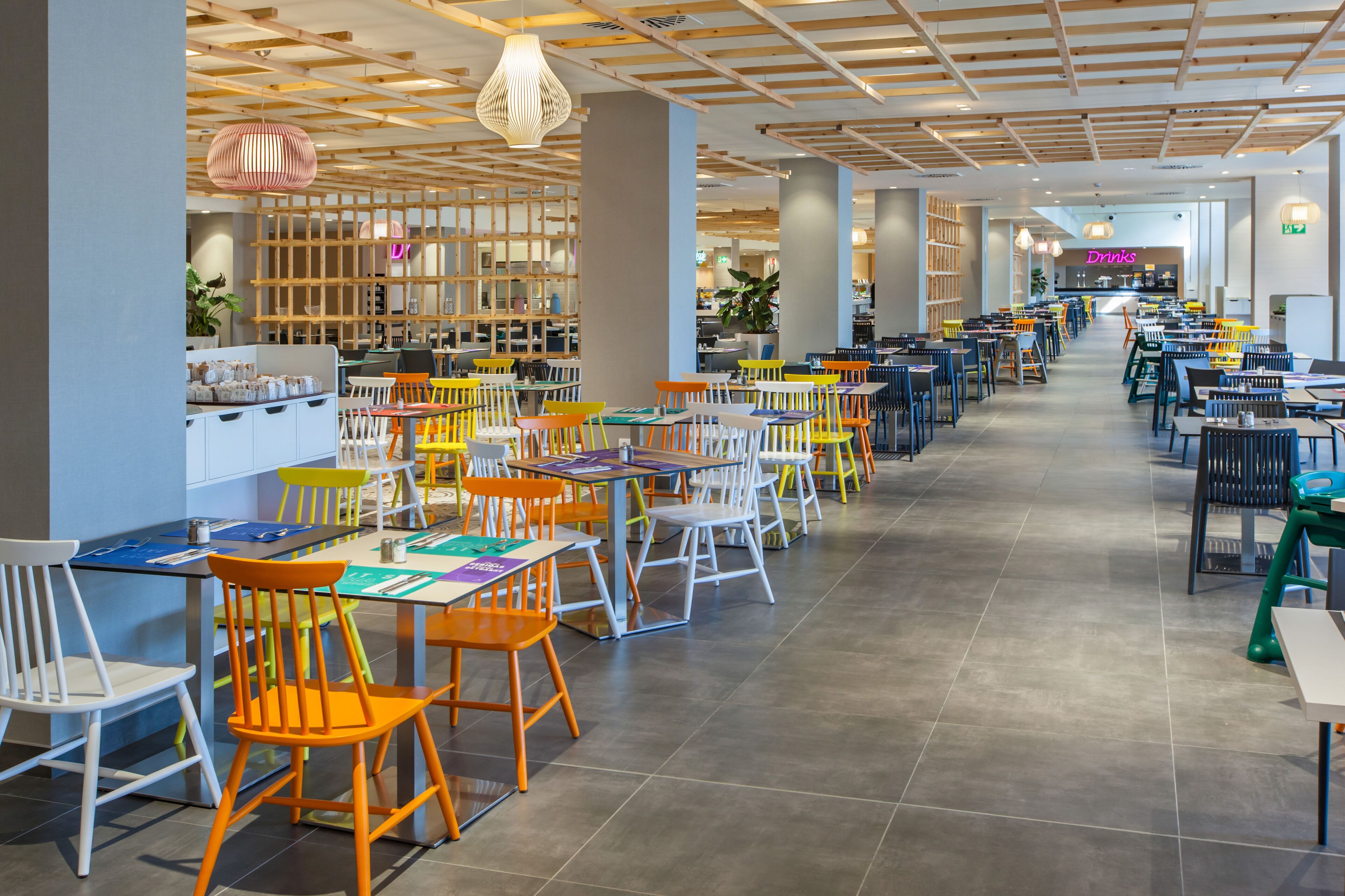 A spacious cafeteria with multiple tables and chairs, wooden beams on the ceiling, and a variety of seating options.