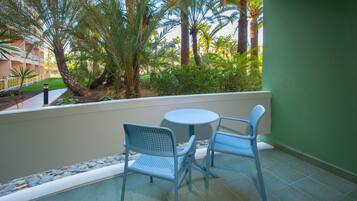 A balcony with two chairs and a table, surrounded by a low stone wall and palm trees.