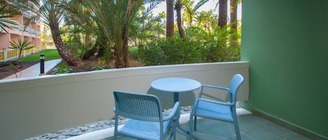 A balcony with two chairs and a table, surrounded by a low stone wall and palm trees.