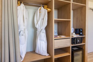 A hotel room with a wooden wardrobe, two white robes hanging on a rack, a small refrigerator, and a microwave on the countertop.