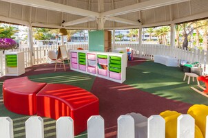 Zona de juegos interior con coloridos contenedores de almacenamiento, una estructura roja para jugar y una valla blanca.