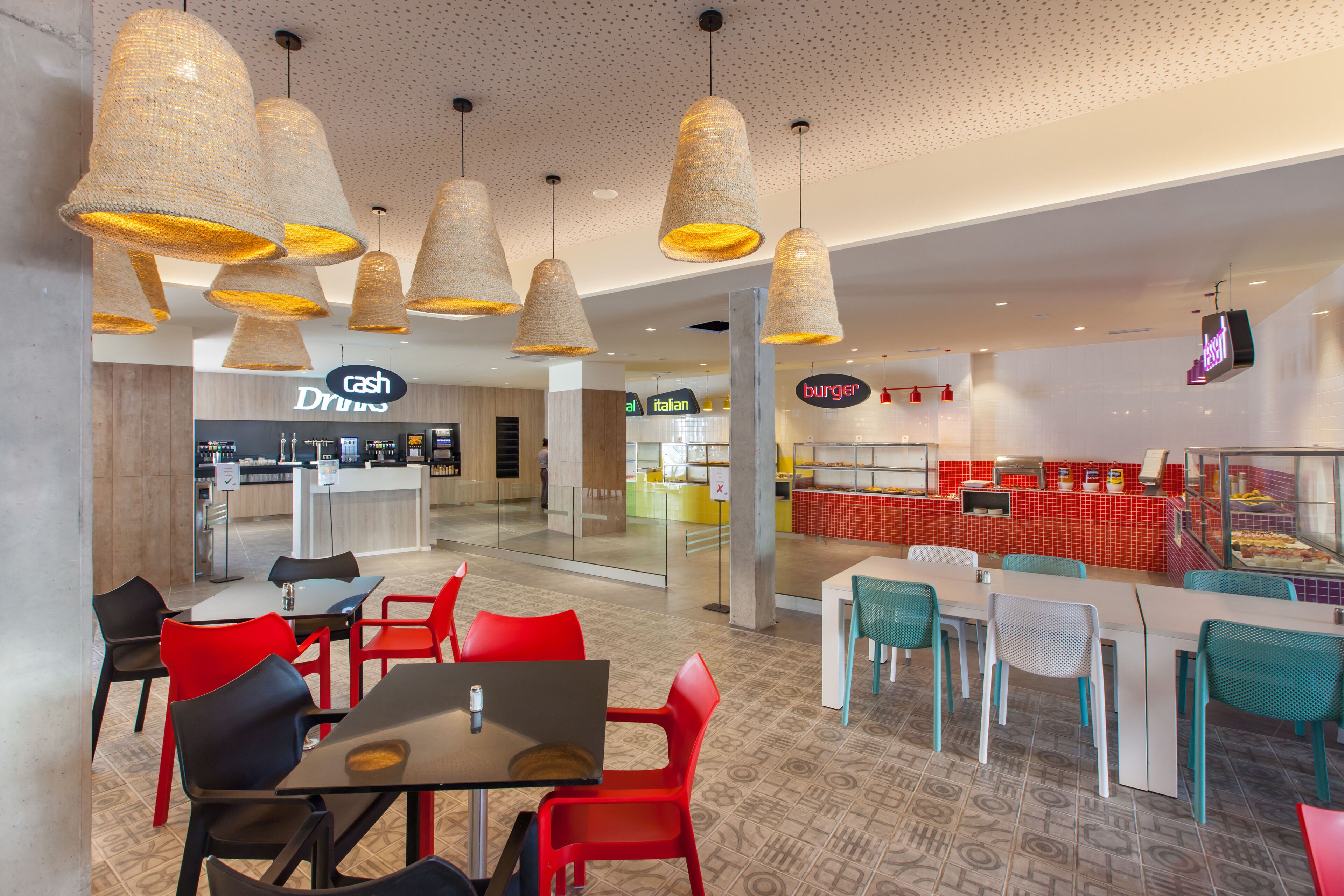A modern restaurant with red and teal chairs, a cash bar, and a burger counter.