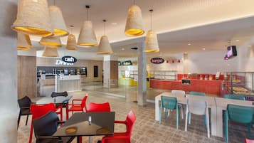 A modern restaurant with red and teal chairs, a cash bar, and a burger counter.