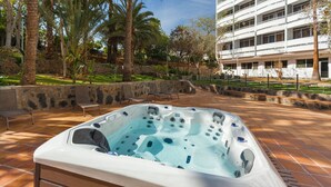 A hot tub in a landscaped outdoor area with stone walls and palm trees.