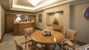 A dining area with a round wooden table, four upholstered chairs, a floral centerpiece, a wooden bar with a mirror, and a framed painting on the wall.