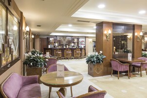Un vestíbulo de hotel con zona de bar, asientos y plantas decorativas.