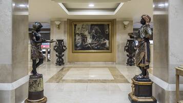 Un vestíbulo con dos estatuas, un cuadro grande y un piso de baldosas.