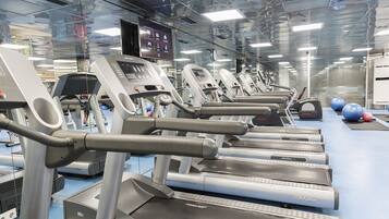 Varias cintas de correr en un gimnasio con piso azul y una pantalla digital encima.