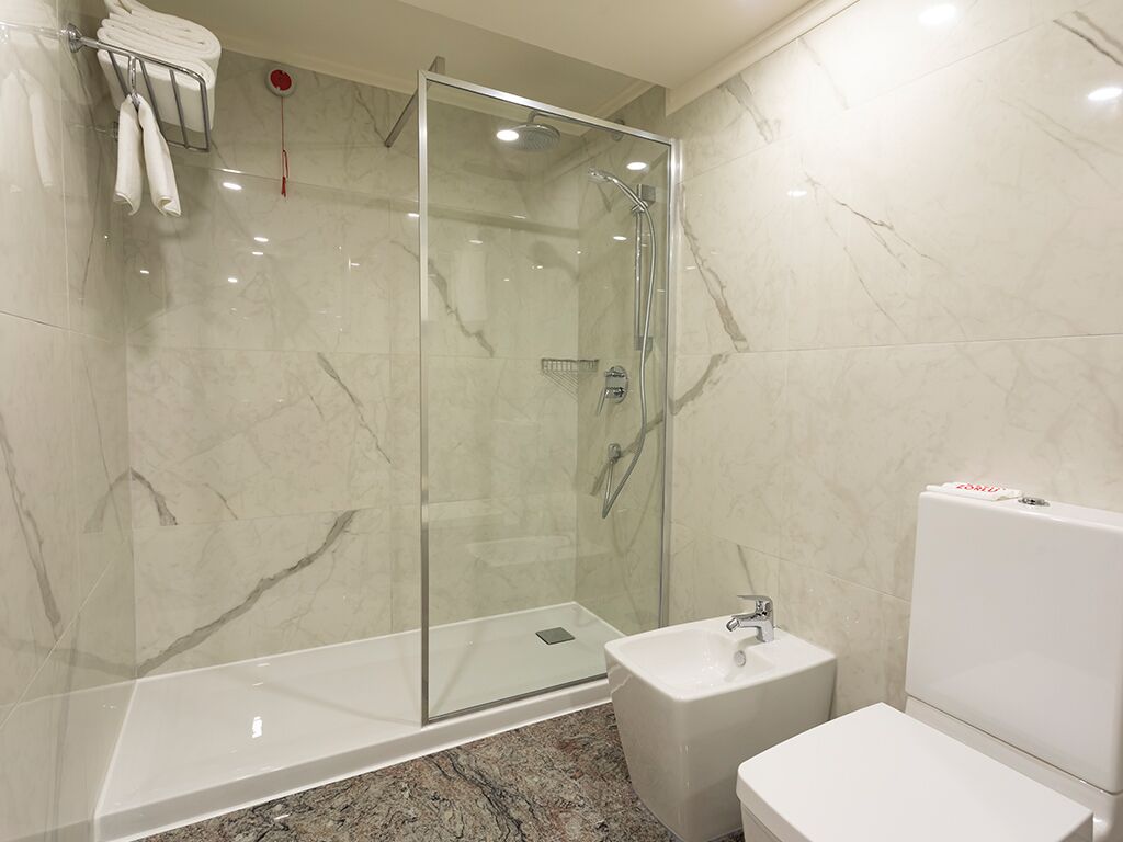 Un baño moderno con ducha envuelta en vidrio, un lavamanos blanco y un inodoro.