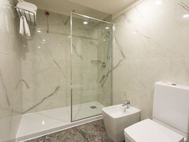 Un baño moderno con ducha envuelta en vidrio, un lavamanos blanco y un inodoro.