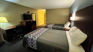 Una habitación de hotel con dos camas, un escritorio con computadora, televisor y lámpara.