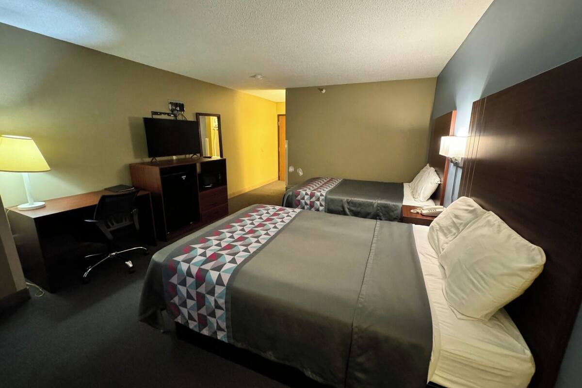 A hotel room with two beds, a desk with a computer, a TV, and a lamp.