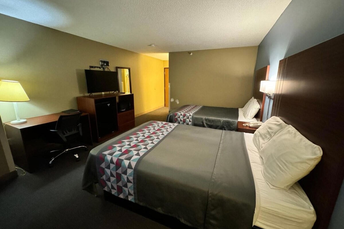 Una habitación de hotel con dos camas, un escritorio con silla, una televisión y una lámpara.