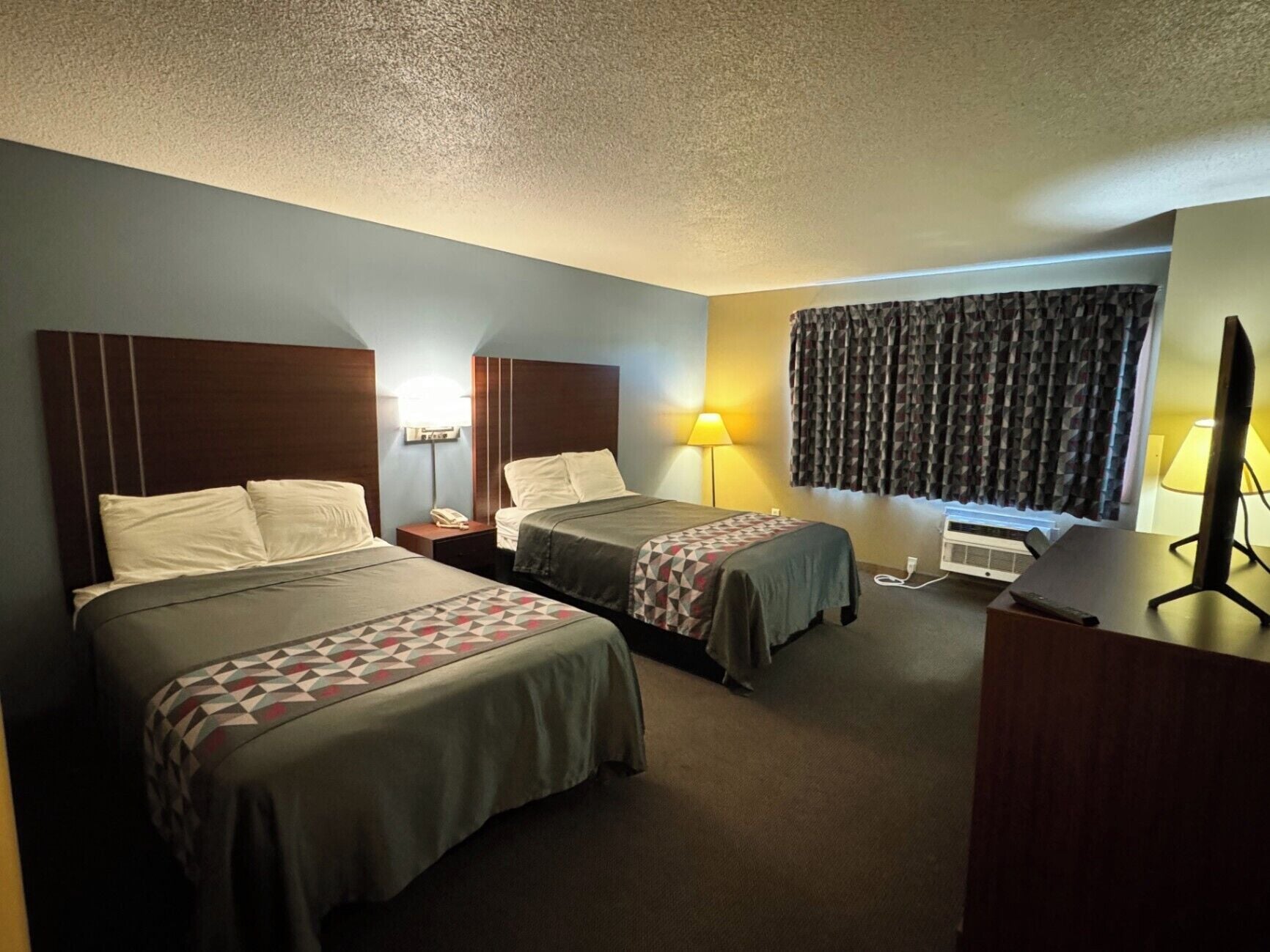 Een hotelkamer met twee bedden, een bureau, een stoel, een televisie en een raam met gordijnen.