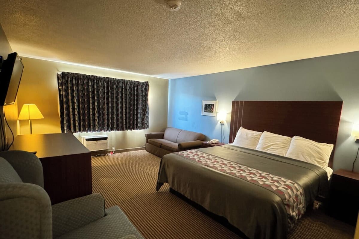 A hotel room with a bed, a sofa, a desk, and a window with curtains.
