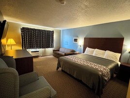 A hotel room with a bed, a sofa, a desk, and a window with curtains.
