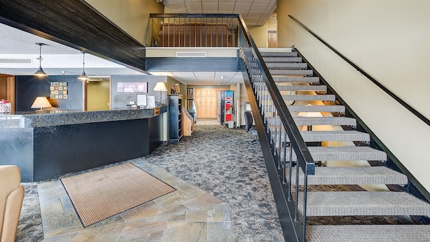 Un vestíbulo de hotel con mostrador de recepción, escalera y área de espera.