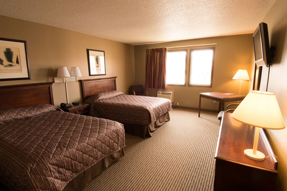 A hotel room with two beds, a desk, a chair, a TV, and a window with curtains.