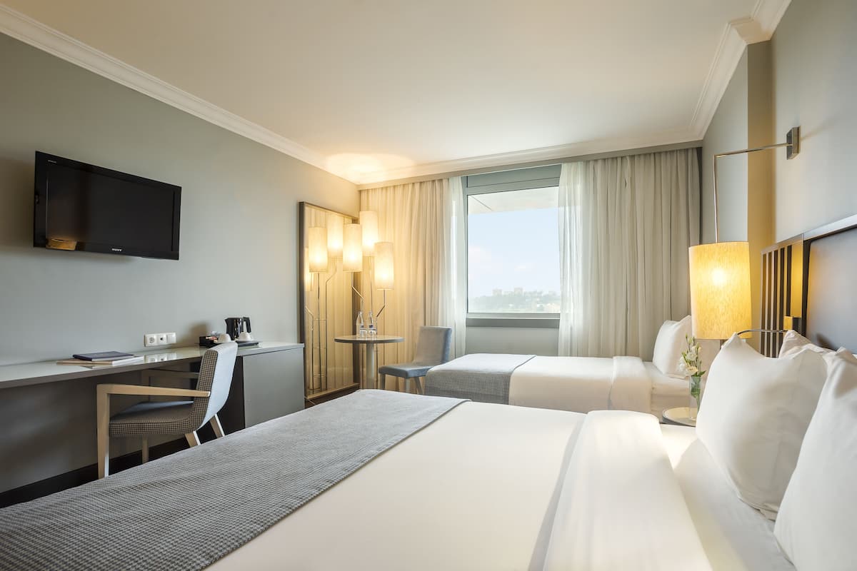 A hotel room with two beds, a desk, a chair, a TV, and a window with curtains.