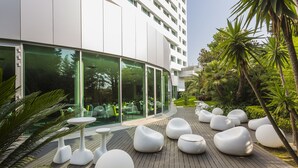 Un espacio exterior moderno con terraza de madera, asientos esféricos blancos y un edificio con cristales que muestra asientos interiores.