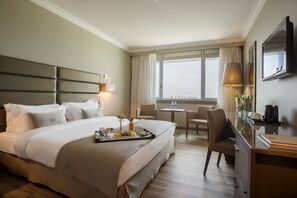 Habitación de hotel con una cama grande, un escritorio, una silla, un televisor y una ventana con vistas a la ciudad.