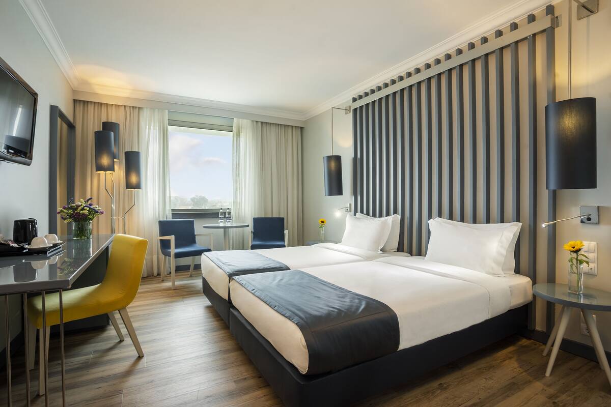 A modern hotel room with a large bed, a desk, a chair, and a small table with a vase of flowers.