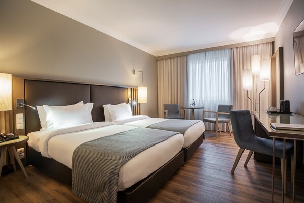 Habitación de hotel con dos camas, un escritorio, una silla y una ventana con cortinas.