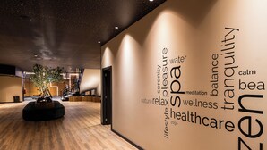 Un interior moderno con suelo de madera, una escultura de árbol central y una pared con palabras relacionadas con el bienestar y la relajación.