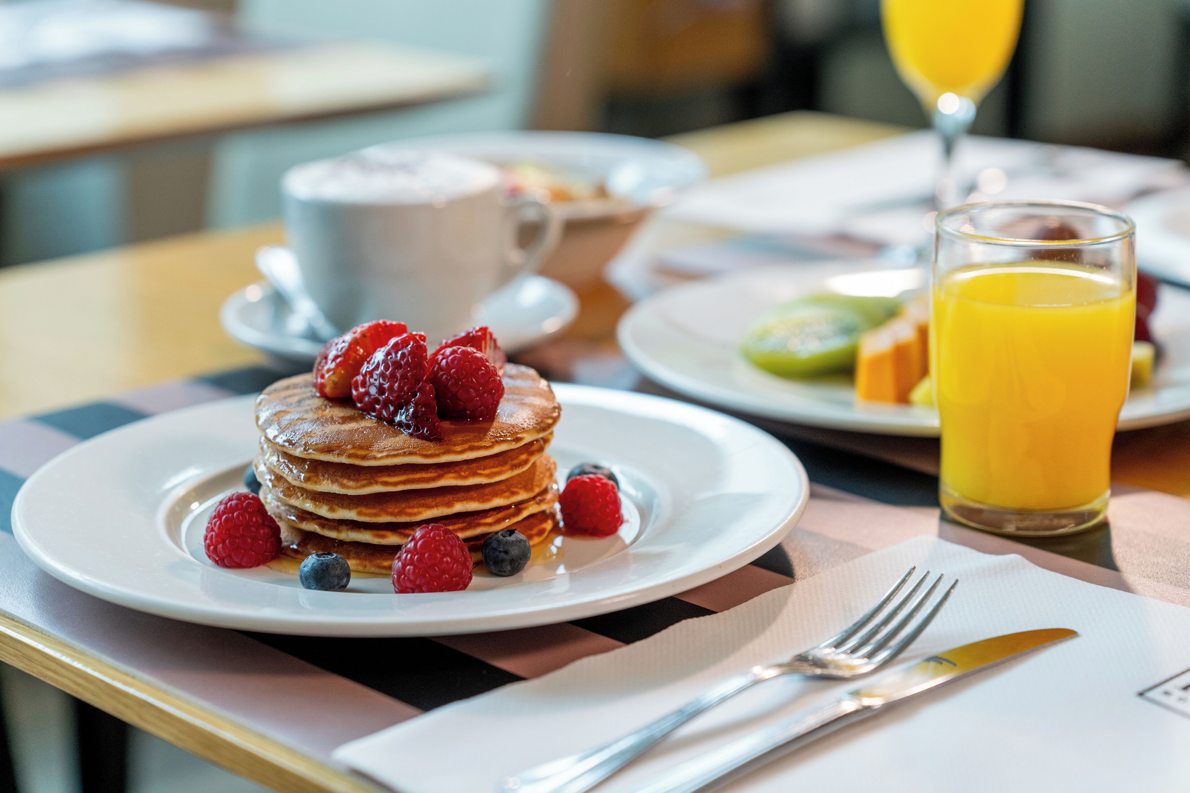 Desayuno con tortitas cubiertas de frutos rojos, una taza de café y un vaso de jugo de naranja.