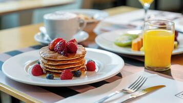 Desayuno con tortitas cubiertas de frutos rojos, una taza de café y un vaso de jugo de naranja.