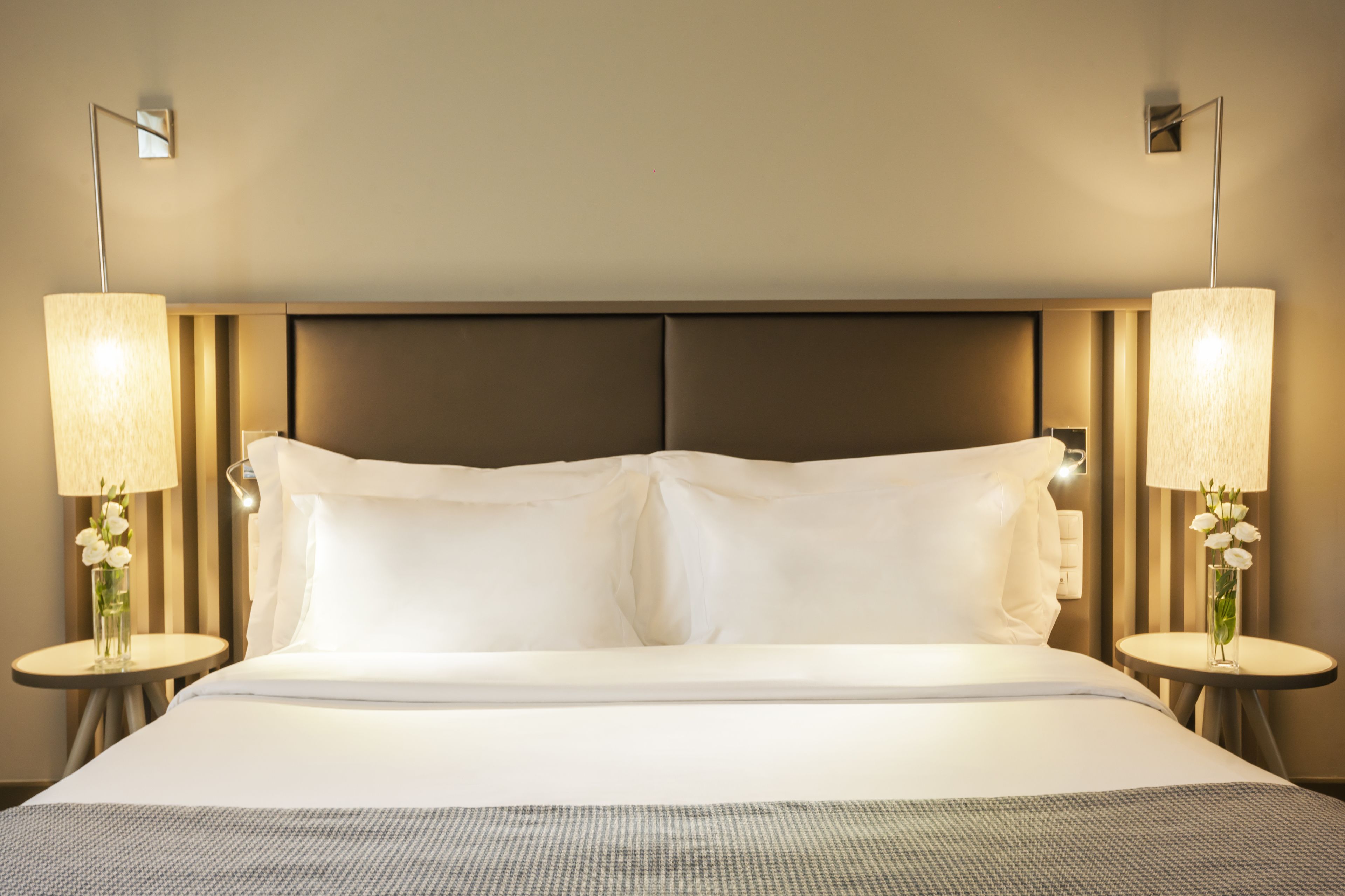 Una habitación de hotel con una cama grande, dos lámparas de noche y un jarrón con flores a cada lado.