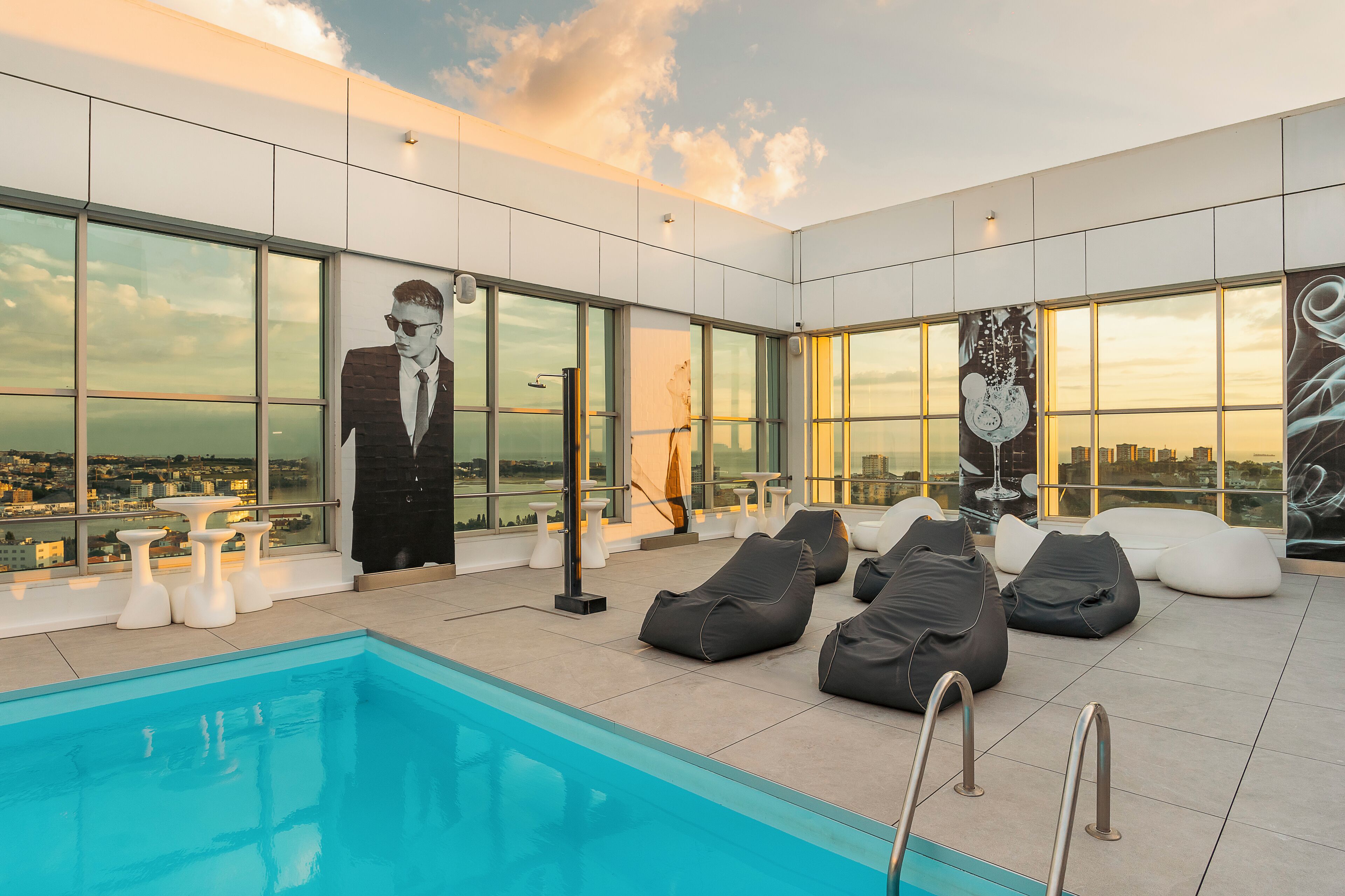 A rooftop pool area with a view of the city, lounge chairs, and a large mural.