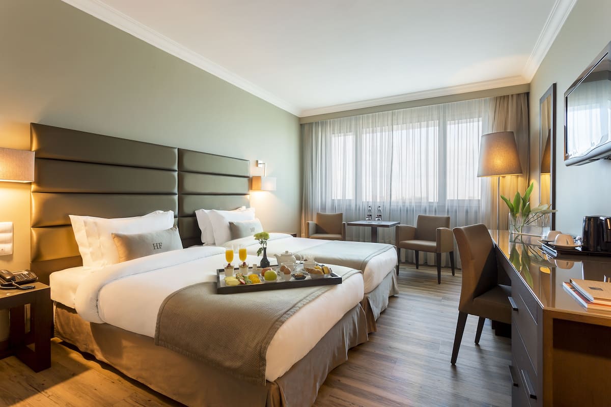 A hotel room with a large bed, a desk, and a chair. There is a tray with breakfast items on the bed.