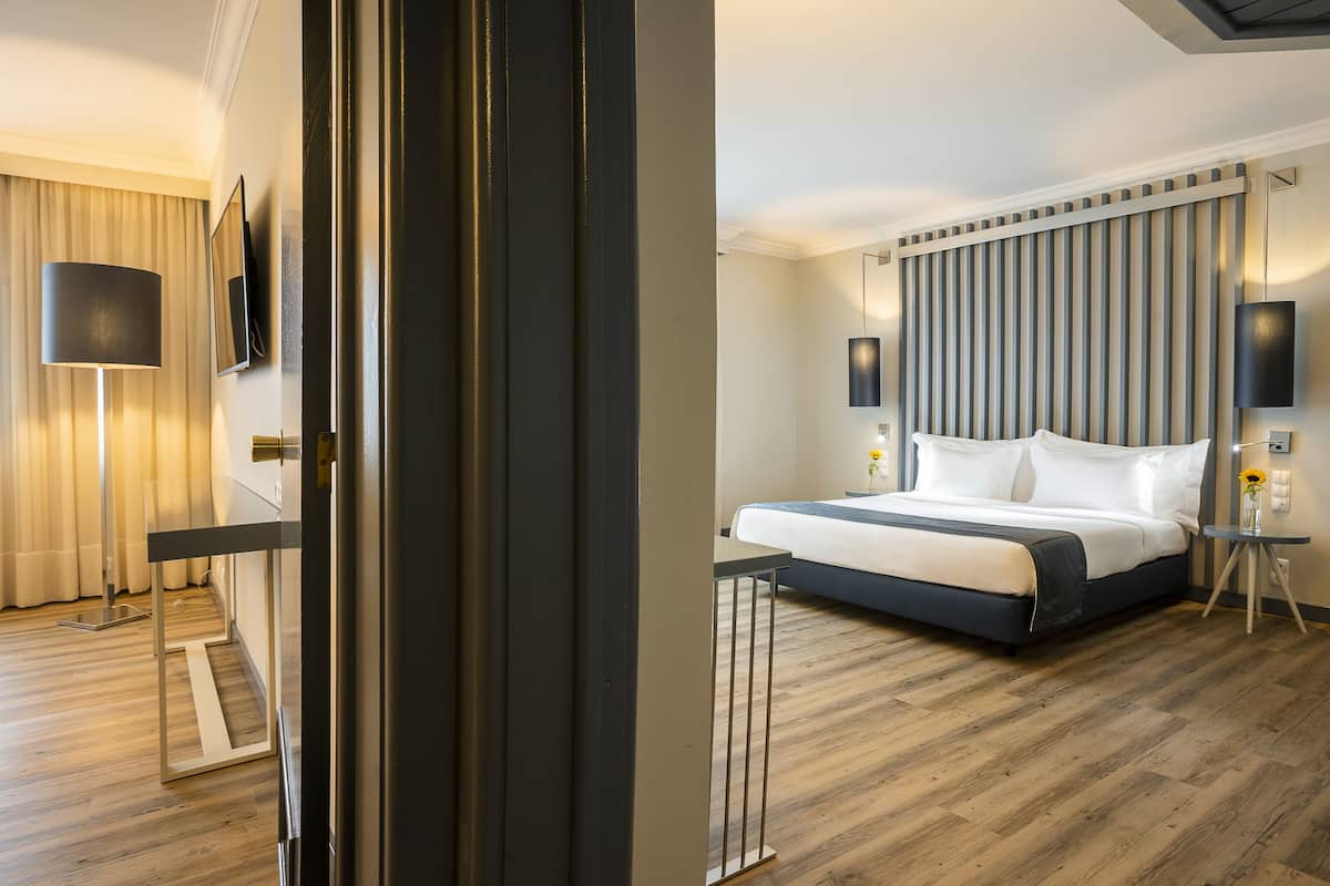 A hotel room with a bed, bedside tables, a lamp, a mirror, and a view of the outside.