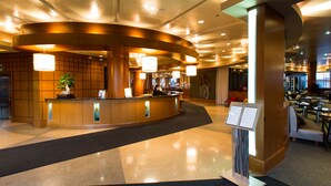 A hotel reception area with a curved reception desk, a digital menu board, and a seating area with tables and chairs. - Brookstreet (Ottawa)
