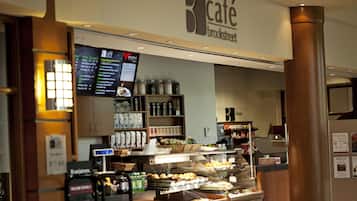 Una cafetería con una pizarra de menú, estantes con frascos y una vitrina con productos de repostería.