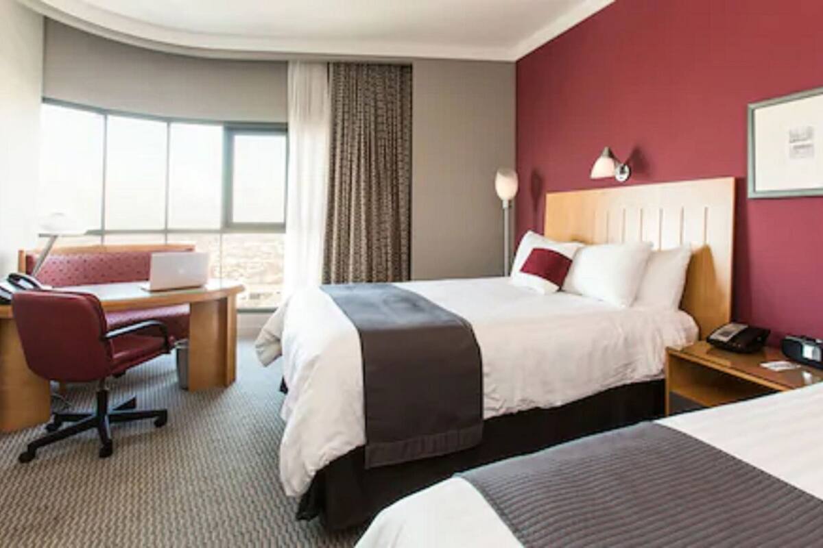 Habitación de hotel con cama, escritorio, silla, lámpara y ventana.
