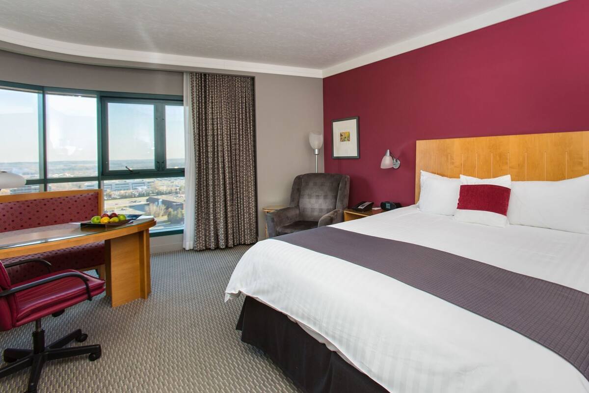 Una habitación de hotel con una cama grande, un escritorio con silla, vistas a la ciudad y una ventana con cortinas.