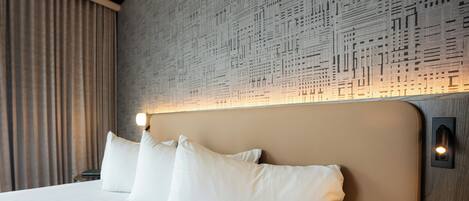 A hotel room with a large bed, white pillows, a headboard with a light fixture, and a patterned wall.