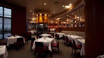 Un restaurante con mesas dispuestas para comer, una zona de bar y vistas a través de amplios ventanales.