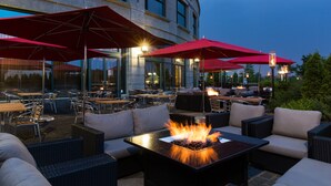 An outdoor seating area with fire pits, red umbrellas, and wicker furniture. - Brookstreet (Ottawa)