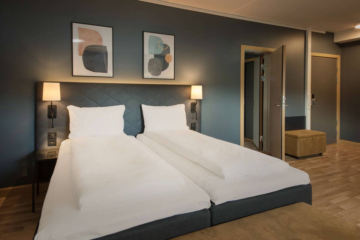 A double bed with white linens, two wall-mounted lamps, and abstract artwork above the bed.