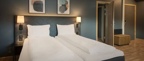 Una cama doble con ropa de cama blanca, dos lámparas de pared y una obra de arte abstracta sobre la cama.