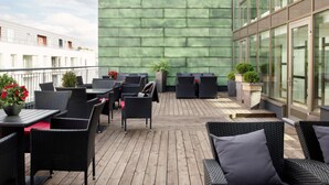 Un patio exterior con mobiliario de mimbre, plantas en macetas y una pared verde.