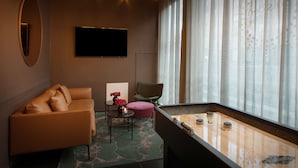 Una habitación acogedora con un sofá, una pequeña mesa con un florero, una silla verde, una mesa de billar y un gran ventanal con cortinas.