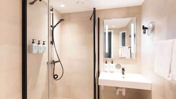 Un baño moderno con cabina de ducha de vidrio, un lavabo blanco y un espejo encima.