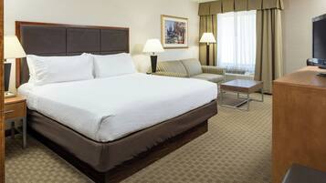 A hotel room with a large bed, a desk, a chair, a television, and a window with curtains.
